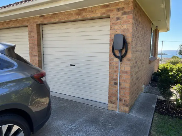 EV charger mounted on a brick garage wall beside a driveway and garage door in Norah Head